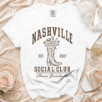 A white t-shirt featuring brown text that reads Nashville Social Club above a cowboy boot graphic.
