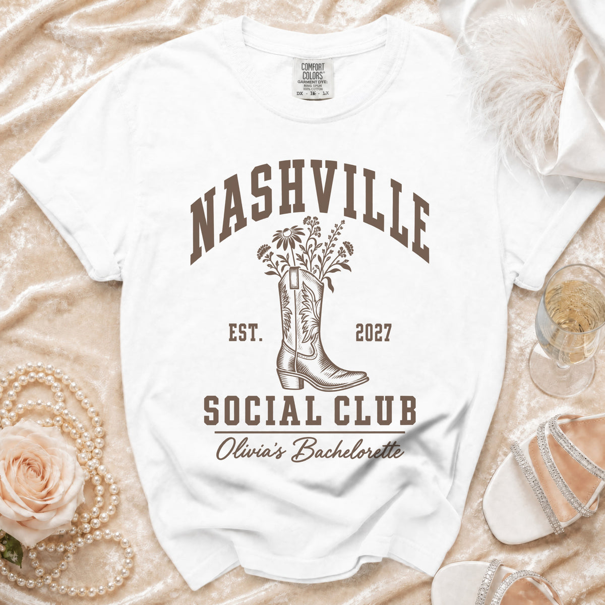 A white t-shirt featuring brown text that reads Nashville Social Club above a cowboy boot graphic.