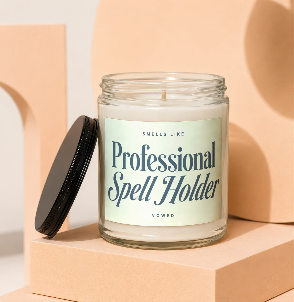 Glass jar candle with black lid, reads "Smells Like Professional Spell Holder".