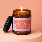 Amber jar candle with lit wick and lid, featuring lavender label with orange text.
