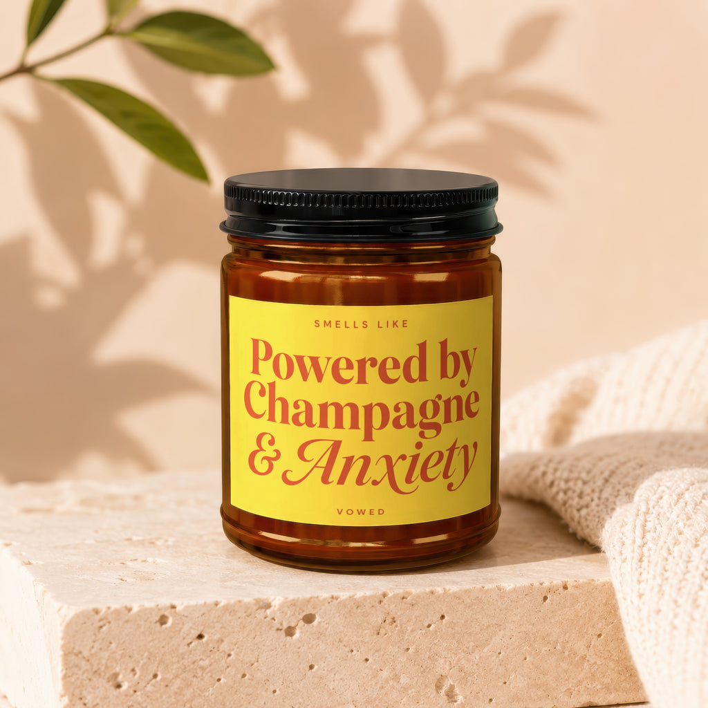 Brown glass candle with yellow label saying "Smells Like Powered by Champagne & Anxiety".