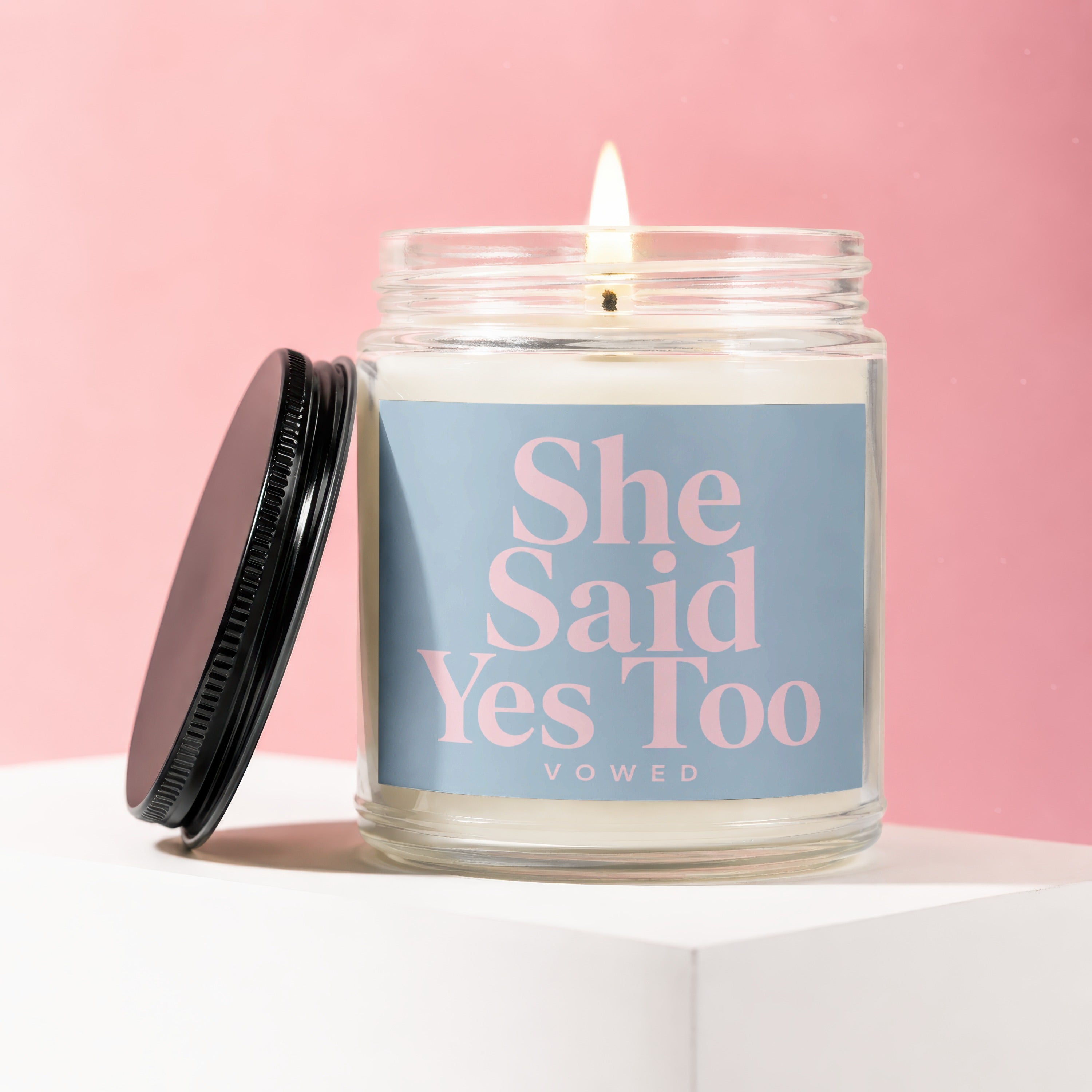 Lit candle in a jar with black lid, featuring "She Said Yes Too" text.
