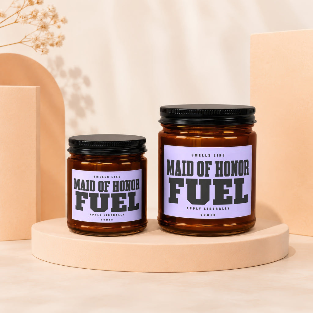 Two amber glass candles with black lids on display stands, labels read "Maid of Honor Fuel."