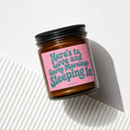 Amber jar candle with pink label reading "Here's to Love and Early Mornings Sleeping In".