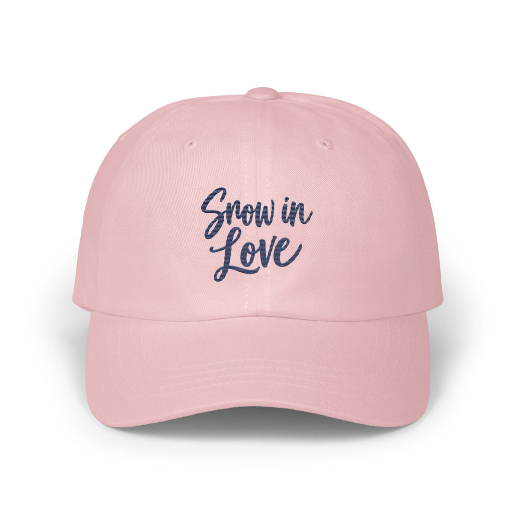 A light pink baseball cap features embroidered blue text reading Snow in Love on the front.