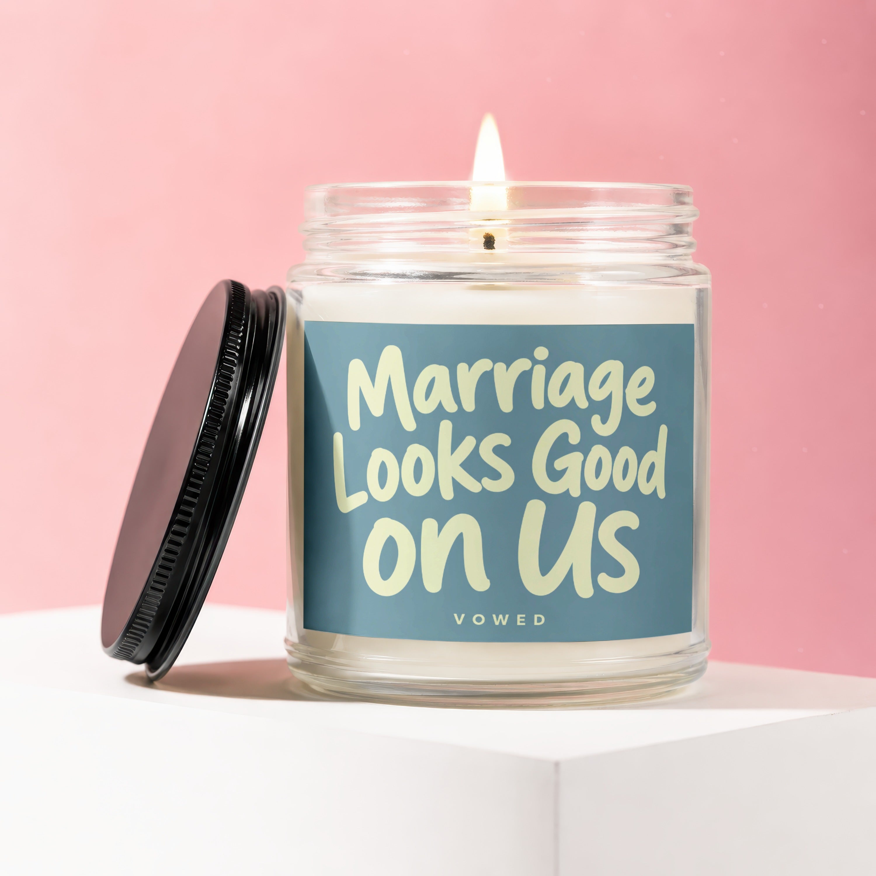 Glass candle with lit wick and "Marriage Looks Good on Us" text.