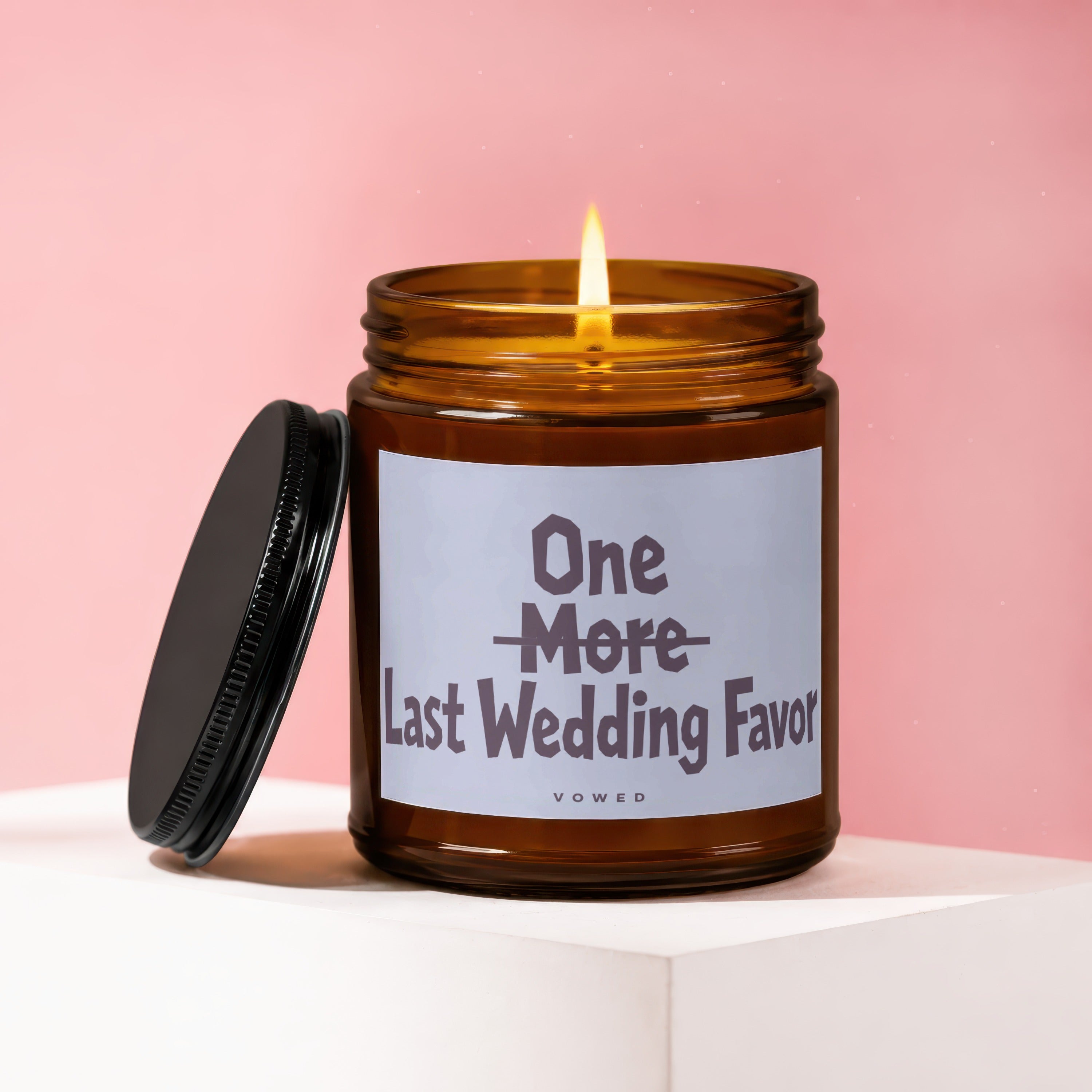 Amber glass candle with lit wick, lid off, reading "One More Last Wedding Favor".