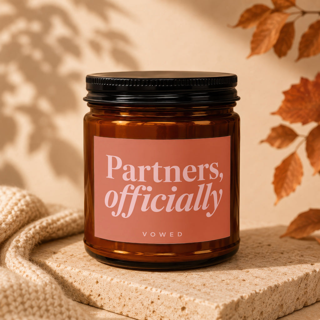Brown glass candle with coral label reading "Partners, officially VOWED".