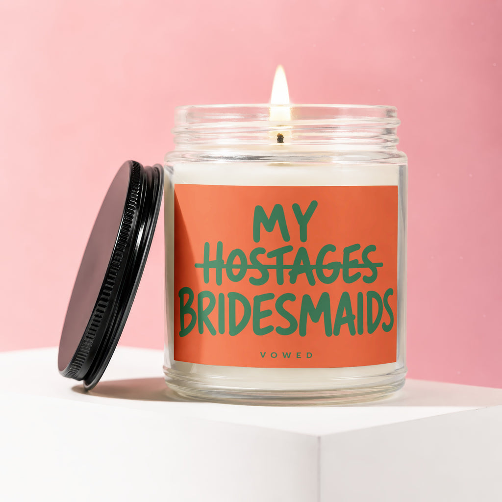 Candle with text "MY HOSTAGES BRIDESMAIDS" on an orange label.
