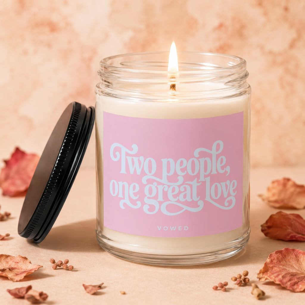 Candle with pink label reading "Two people, one great love" on a beige background.