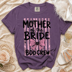 Purple t-shirt featuring the text Mother of the Bride Boo Crew over pink stripes and spiderwebs.