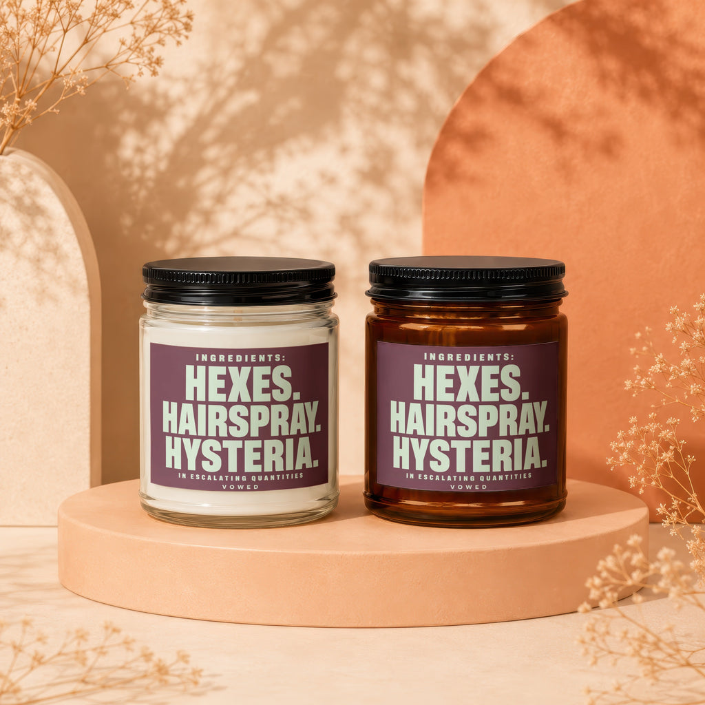 Two candles with purple labels read "Hexes. Hairspray. Hysteria. In Escalating Quantities. Vowed."
