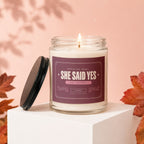Candle with "She Said Yes" label, lit and next to its lid.