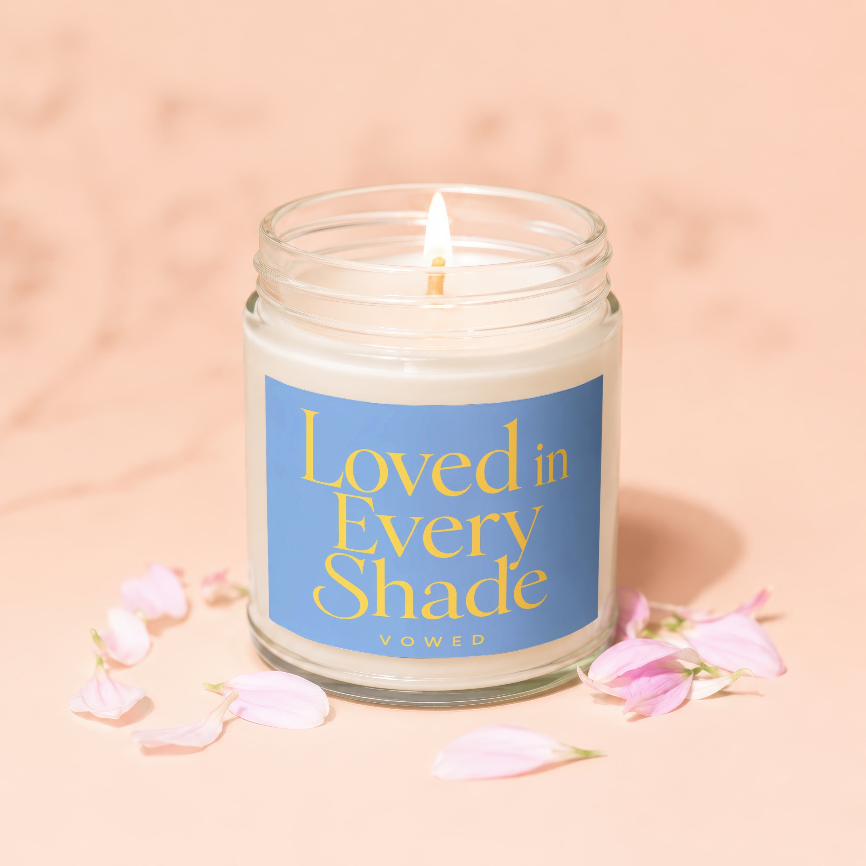 Lit scented candle in glass jar with blue label reading "Loved in Every Shade".