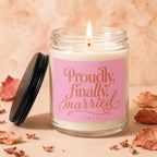 Glass candle with lit wick and pink label that reads "Proudly, finally married."