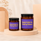 Two amber glass candles with black lids, one larger than the other, labeled "Stuck With Me, Maid of Honor."