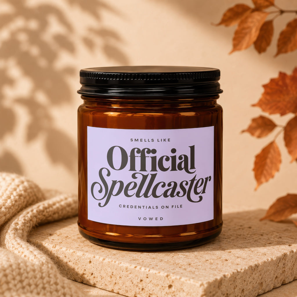 Amber jar candle with black lid, reads "Official Spellcaster" and other text.