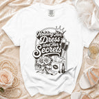 White t-shirt with "Holding Her Dress and Her Secrets" graphic, crown, champagne, flowers, lipstick.