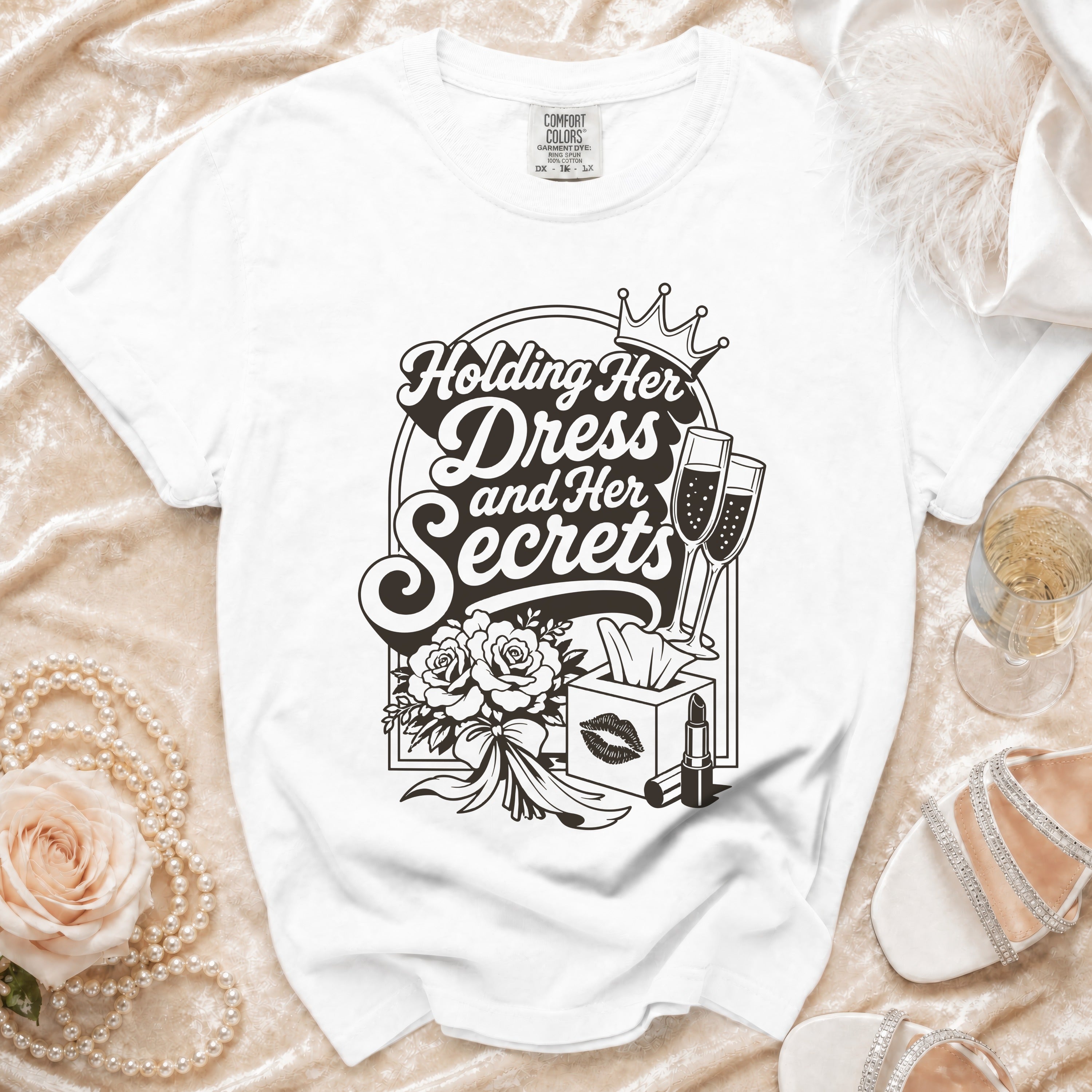 White t-shirt with "Holding Her Dress and Her Secrets" graphic, crown, champagne, flowers, lipstick.