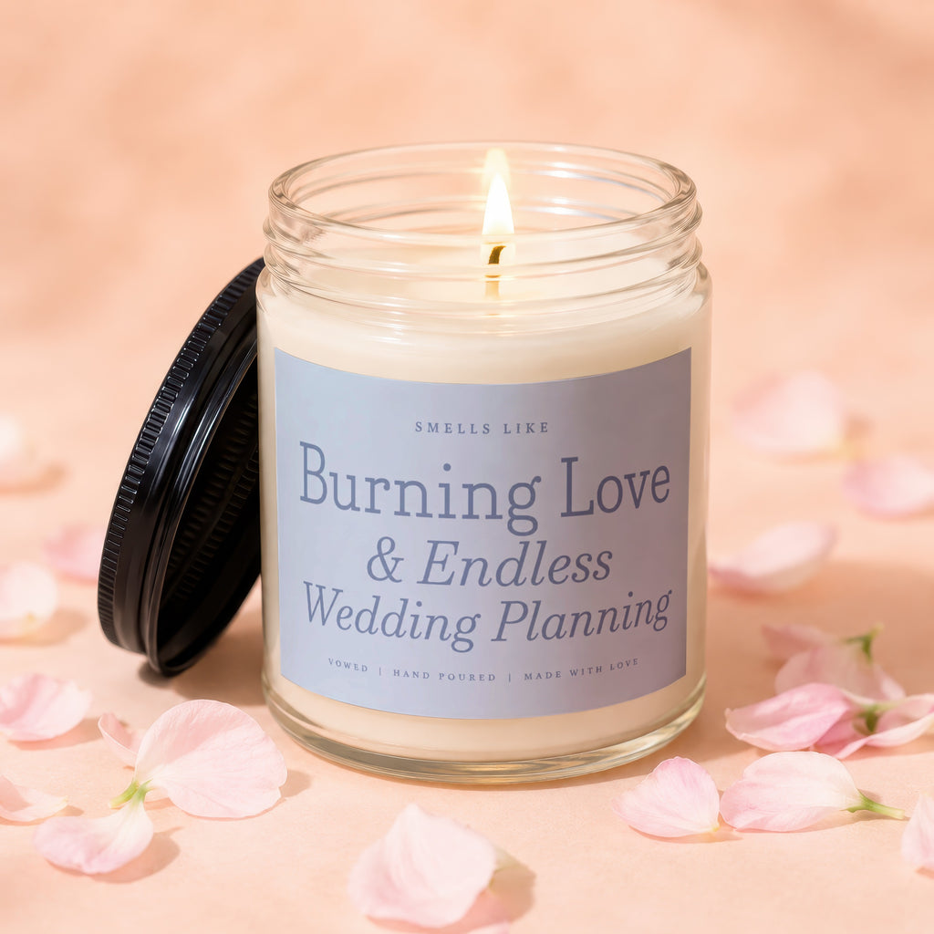 Glass candle with a lit wick, featuring a label reading "Burning Love & Endless Wedding Planning."