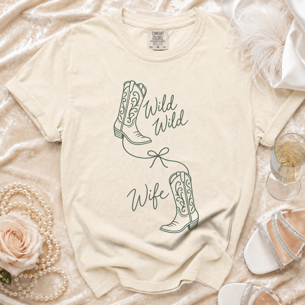 A cream-colored t-shirt with green line drawings of cowboy boots and the text Wild Wild Wife.