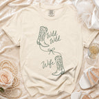 A cream-colored t-shirt with green line drawings of cowboy boots and the text Wild Wild Wife.