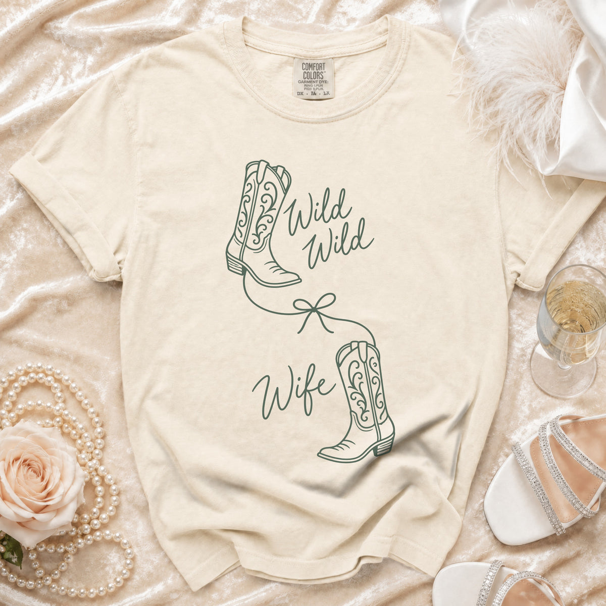 A cream-colored t-shirt with green line drawings of cowboy boots and the text Wild Wild Wife.