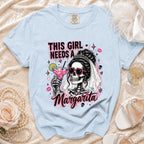 Light blue t-shirt with graphic of skeleton bride holding margarita and text "THIS GIRL NEEDS A MARGARITA".