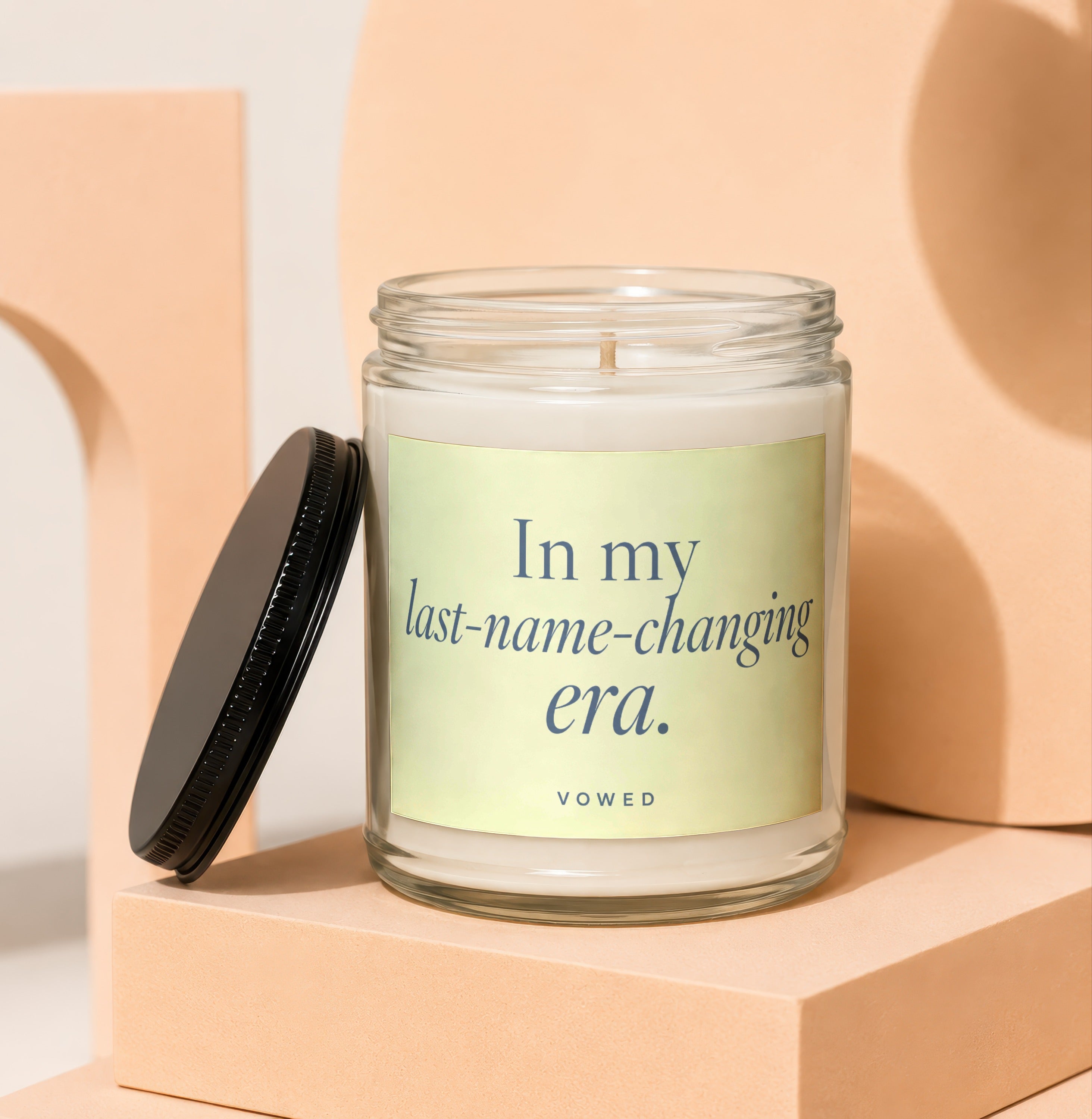 A glass candle with a black lid and text "In my last-name-changing era. VOWED".