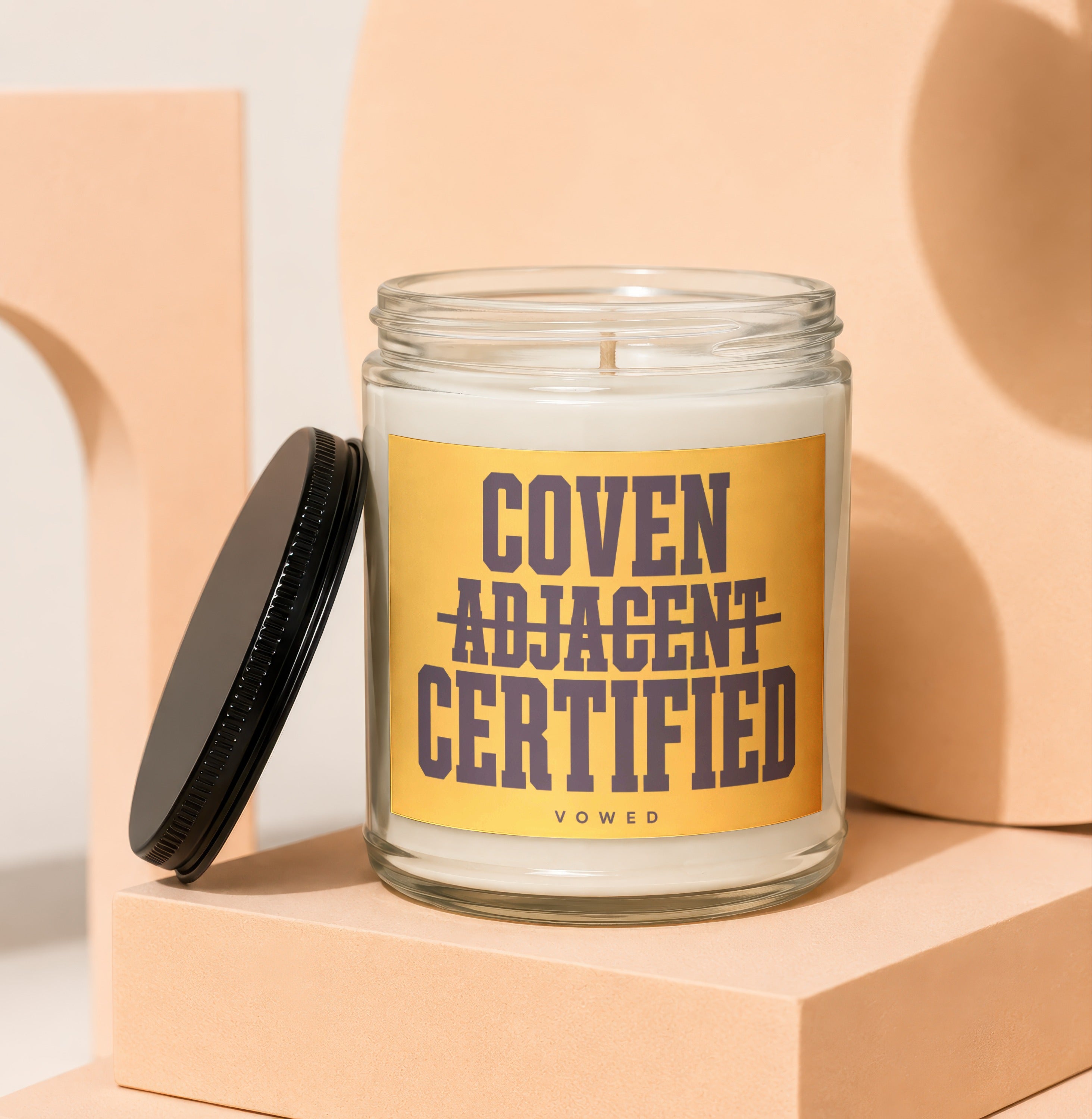 Glass candle with yellow label reading "Coven Adjacent Certified Vowed".