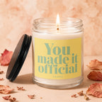 Lit candle in glass jar with yellow label reading "You made it official"