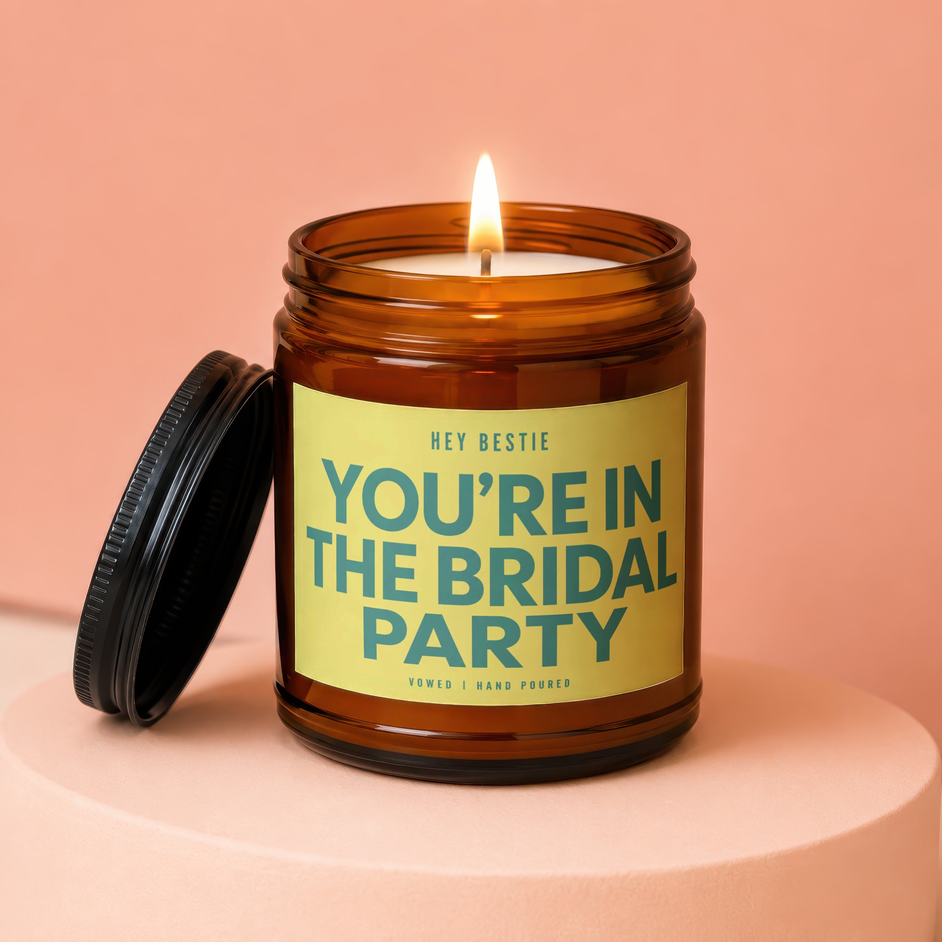 Amber jar candle with lit wick, lid ajar, reads "YOU'RE IN THE BRIDAL PARTY".