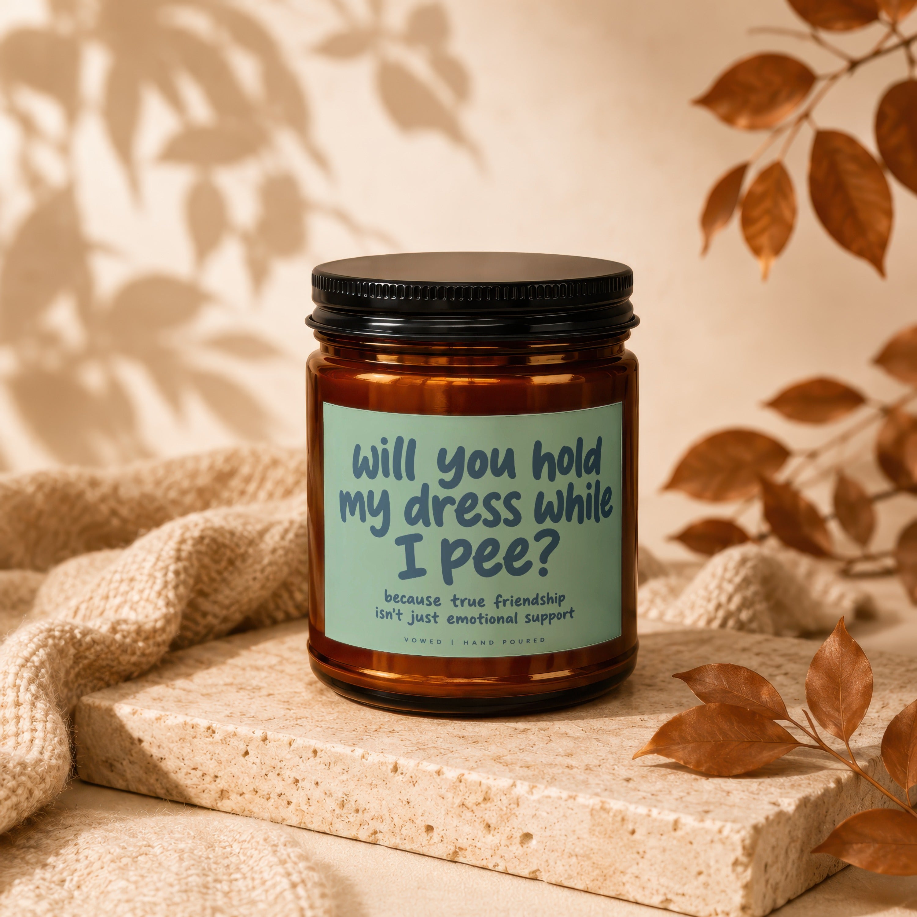 Amber jar candle with black lid reads "Will you hold my dress while I pee?"
