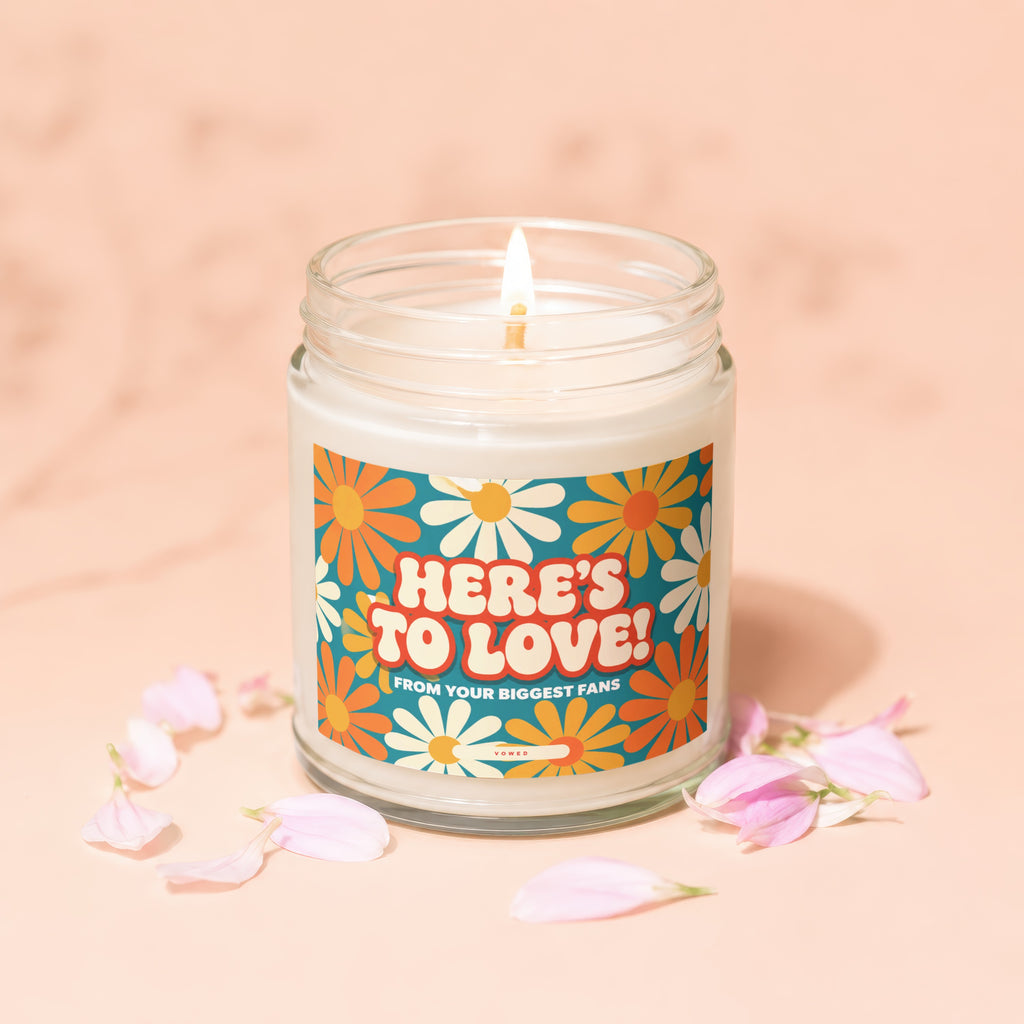 Glass jar candle with lit wick and "HERE'S TO LOVE! FROM YOUR BIGGEST FANS" text.
