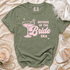 Olive green t-shirt with pink "Mother of the Bride Era" text and cocktail graphic.