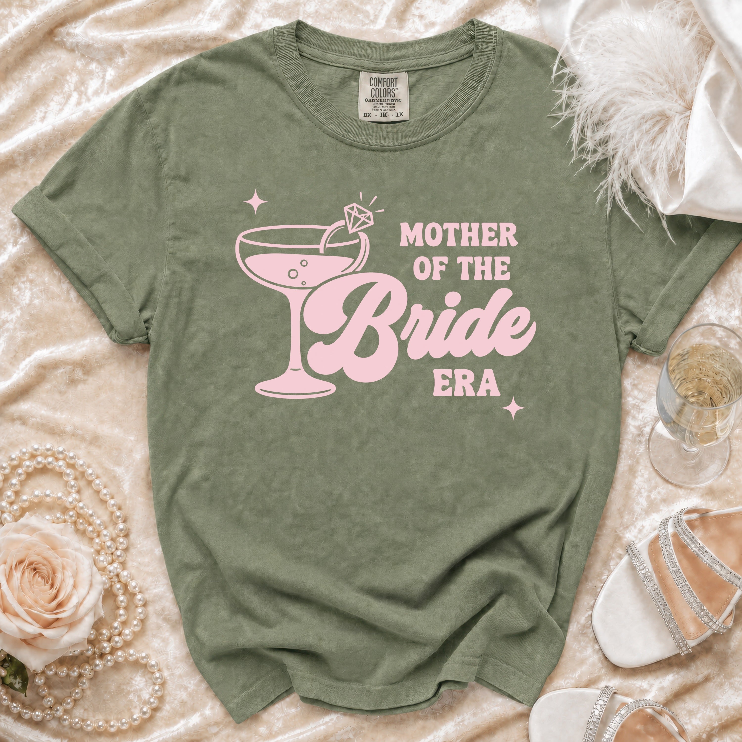 Olive green t-shirt with pink "Mother of the Bride Era" text and cocktail graphic.