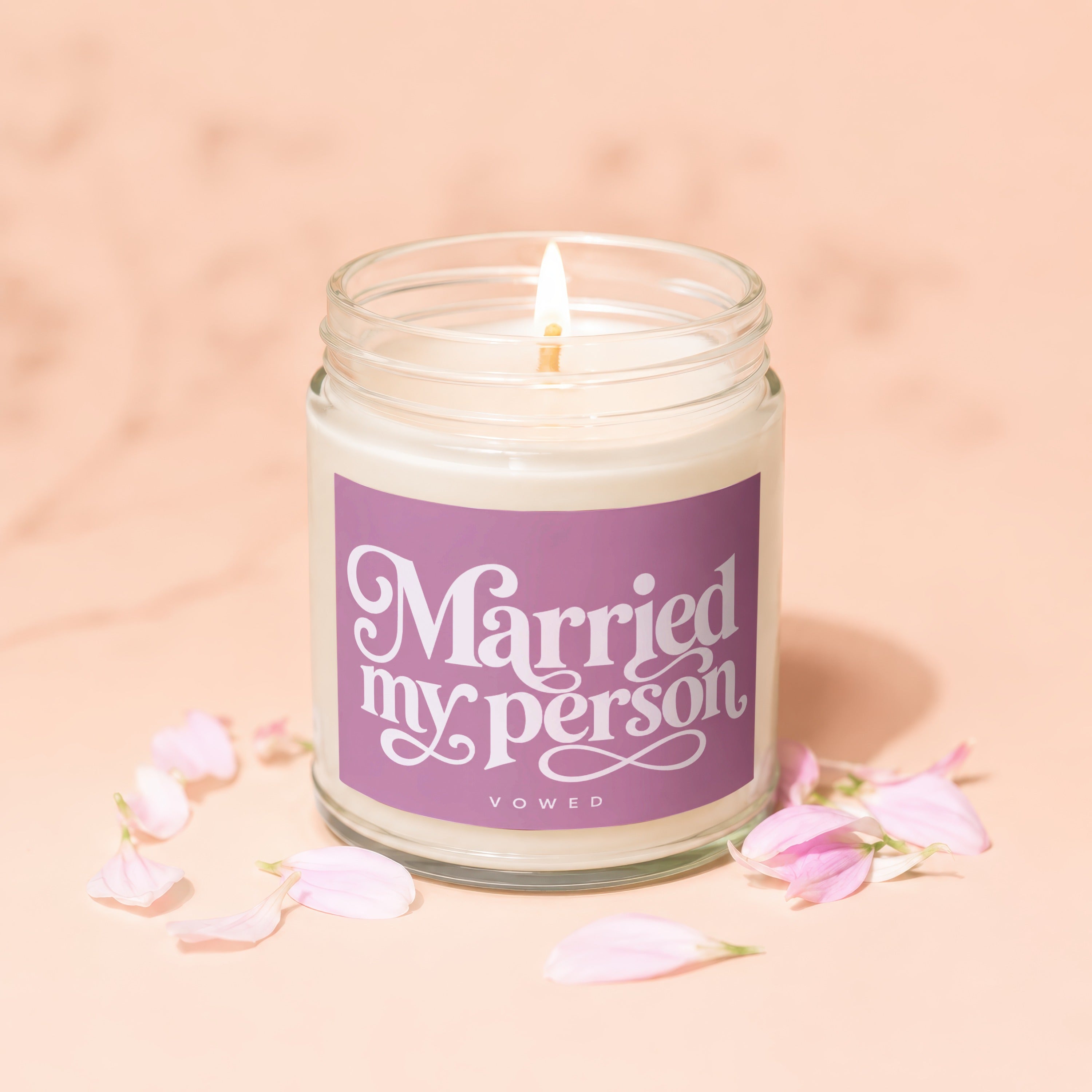 Jar candle with "Married my person" text on purple label, lit flame, and pink petals.