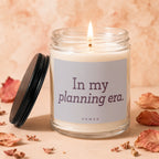 Glass candle with lit wick, labeled "In my planning era. VOWED."
