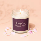 Candle with "Ring On, Heart Full. VOWED" text on label, surrounded by petals.