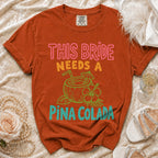 Orange t-shirt with text "THIS BRIDE NEEDS A PINA COLADA" and coconut graphic.