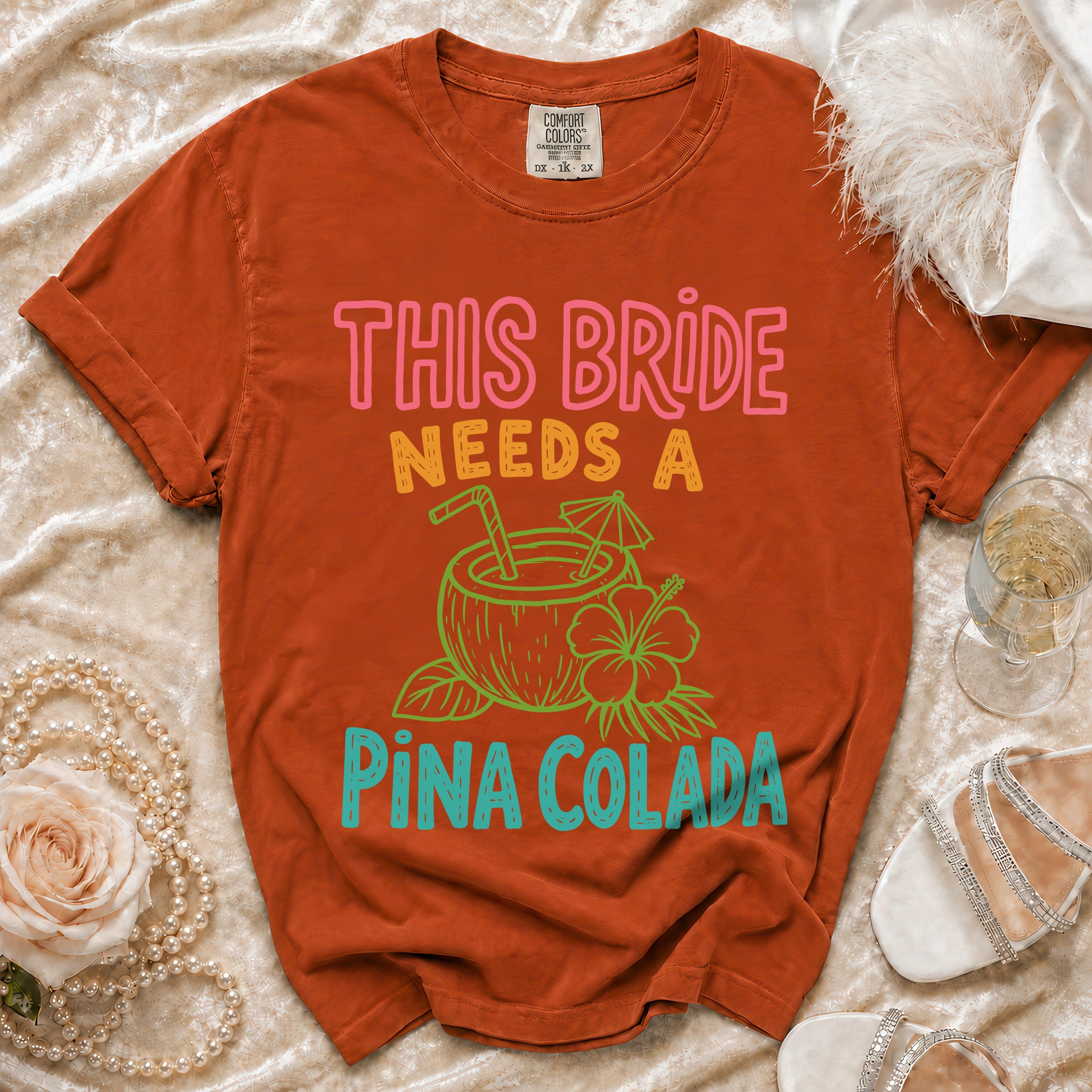 Orange t-shirt with text "THIS BRIDE NEEDS A PINA COLADA" and coconut graphic.