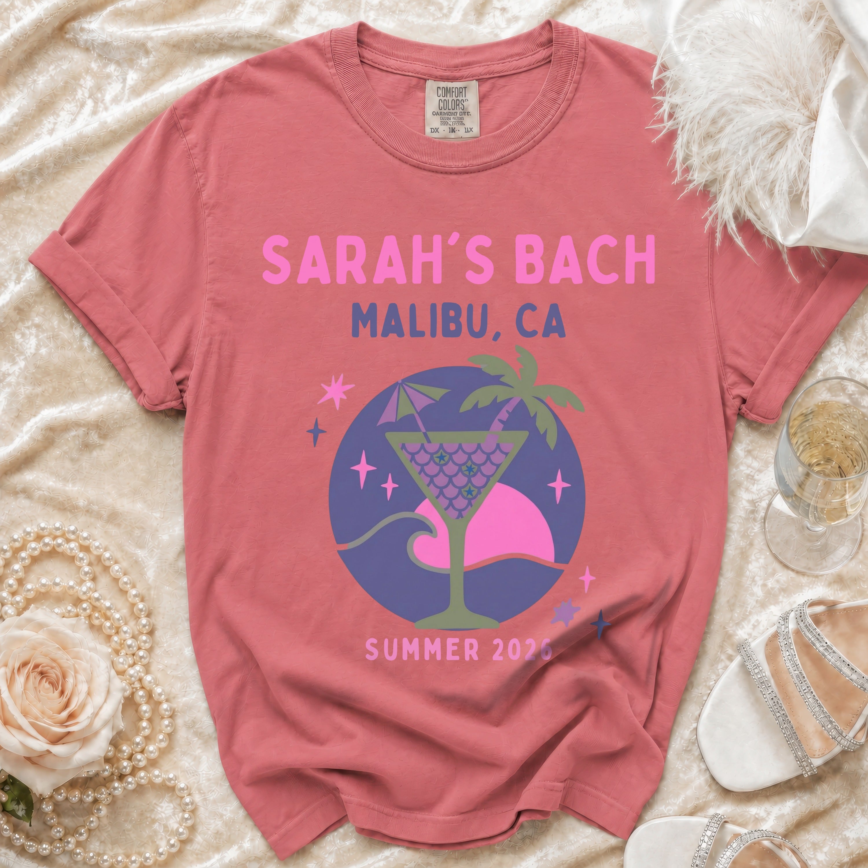 Pink graphic tee with "SARAH'S BACH MALIBU, CA SUMMER 2026" and a cocktail design.