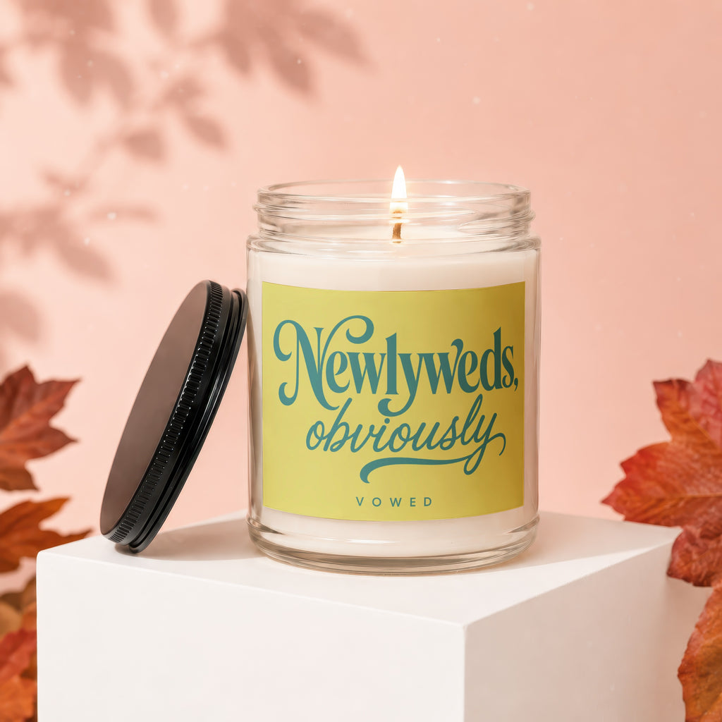 Glass candle with yellow label reading "Newlyweds, obviously," on a white block.