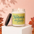 Glass candle with yellow label reading "Newlyweds, obviously," on a white block.