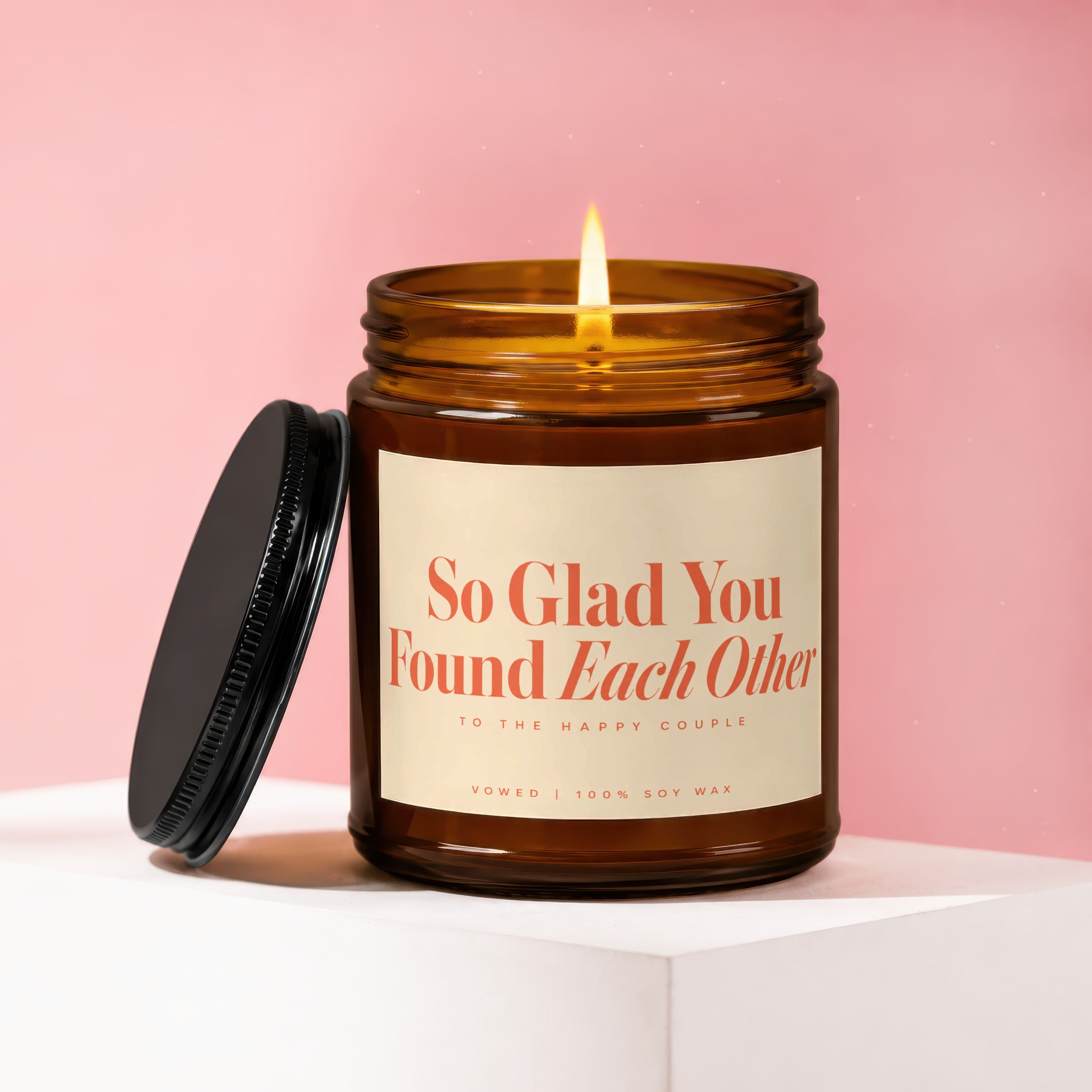 Amber jar candle with lit wick labeled "So Glad You Found Each Other"