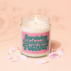 Candle with a pink label that reads "Surviving Celebrating Forever" surrounded by petals.
