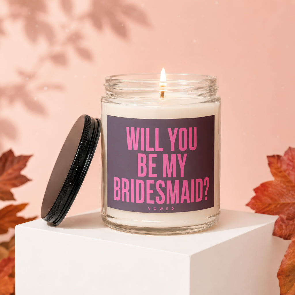Glass candle with pink text "WILL YOU BE MY BRIDESMAID?" on dark purple label.