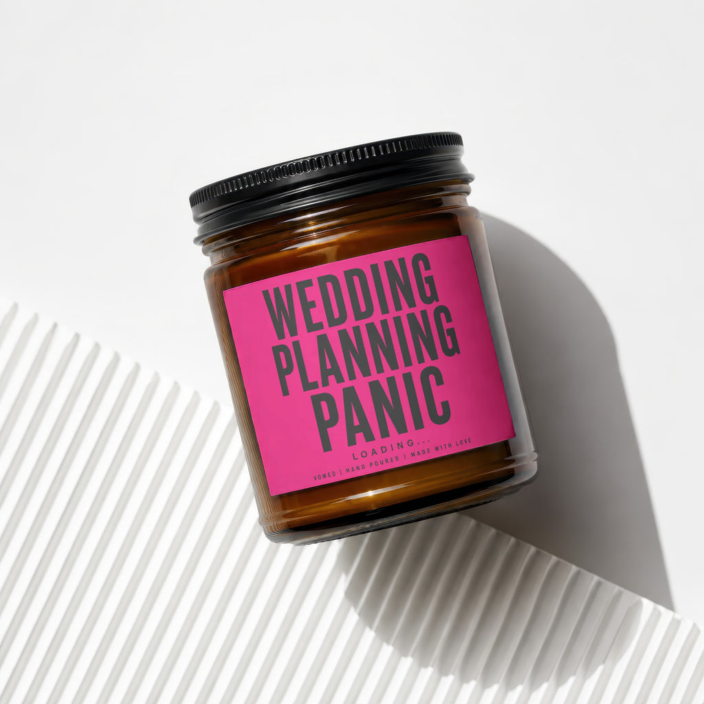 Amber glass candle with bright pink label reading "WEDDING PLANNING PANIC LOADING..."