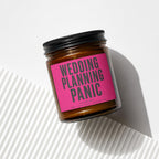 Amber glass candle with bright pink label reading "WEDDING PLANNING PANIC LOADING..."