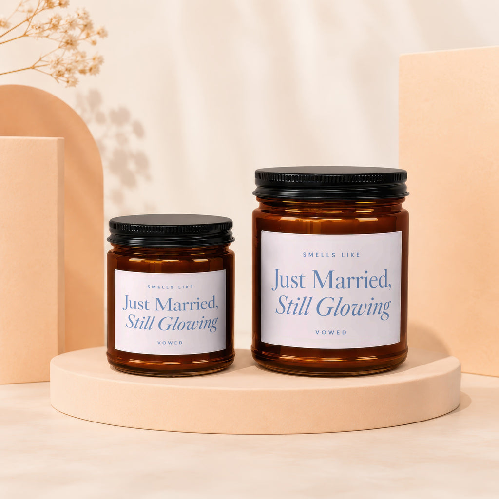 Two amber glass candles with black lids, text reads "Just Married, Still Glowing".